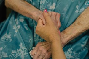 A nurse holds hands with a resident at a skilled nursing facility