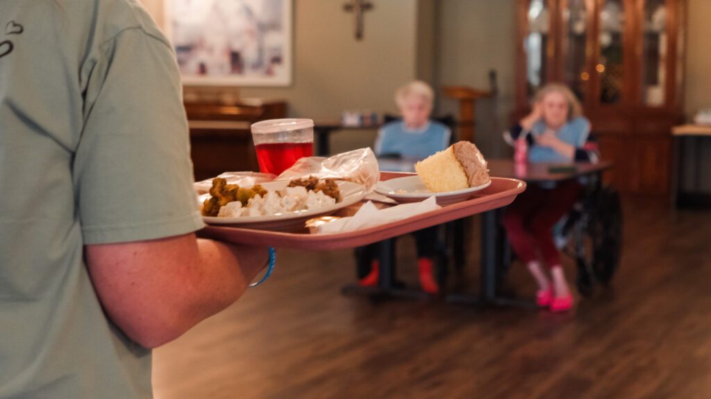 A nurse bringing food to a dining table at a skilled nursing facility
